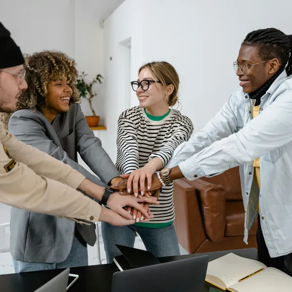 A group of people putting their hands together in support of each other and smiling